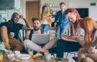 Group of young people spending their time in common living room. Checking their gadgets to catch up with latest news or messages or studying. They are friends who sharing living space.