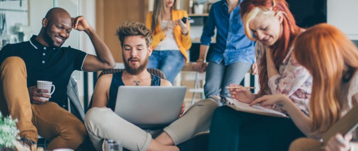 Group of young people spending their time in common living room. Checking their gadgets to catch up with latest news or messages or studying. They are friends who sharing living space.